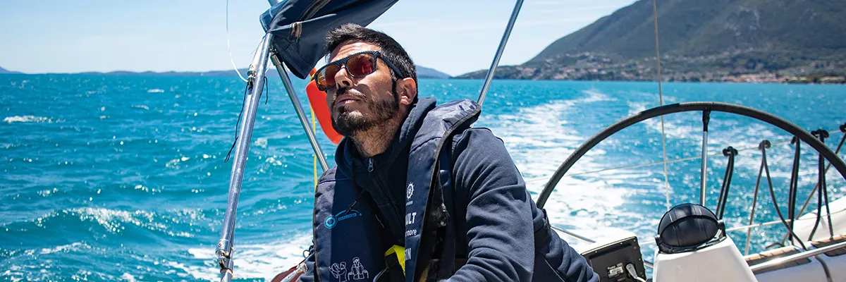 Man practising winching on a sailing yacht during an RYA training course, with blue sea and mountains in the background